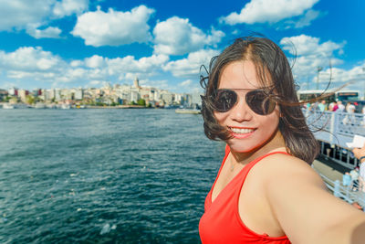 Portrait of smiling woman wearing sunglasses taking selfie while standing against sky