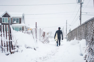 Surfer walks away from the beach during a winter snow storm in maine