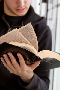 Midsection of young man reading bible at home 