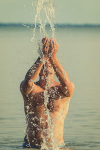 Shirtless man splashing water while standing in sea