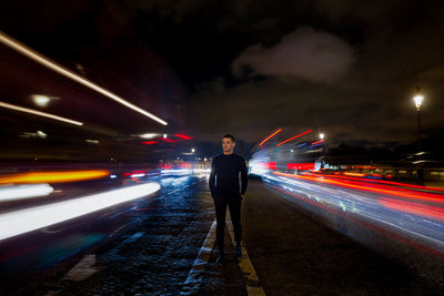 Man standing amidst light trails on road at night