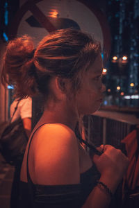 Close-up portrait of woman looking at illuminated camera at night