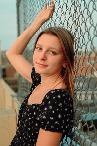 Portrait of young woman standing against chainlink fence