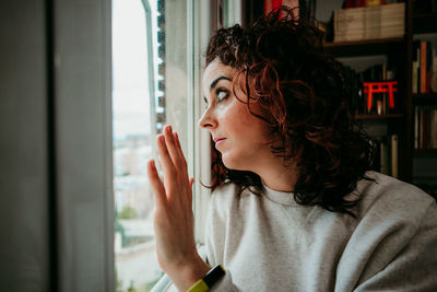 Portrait of young woman looking through window at home