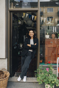 Portrait of smiling female entrepreneur leaning with arms crossed at store doorway