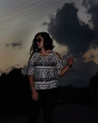 Young woman standing against cloudy sky