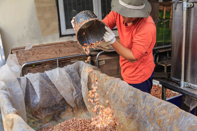 Midsection of man pouting cocoa seeds in container