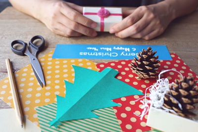 Cropped image of person holding christmas present by decorations on table