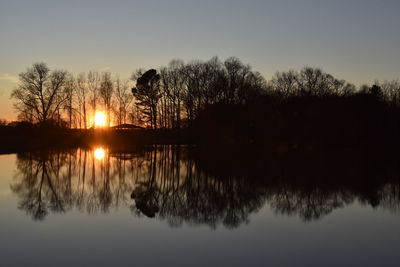 Silhouette trees by lake against sky during sunset