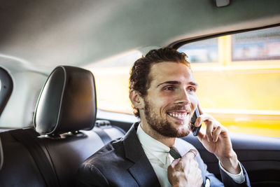 Smiling businessman talking on phone while traveling in car