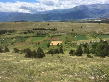 Scenic view of field by houses and mountains against sky