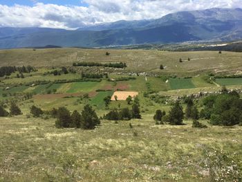 Scenic view of field by houses and mountains against sky