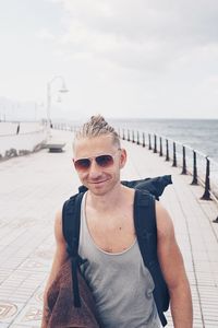 Portrait of smiling young man standing on retaining wall against sea