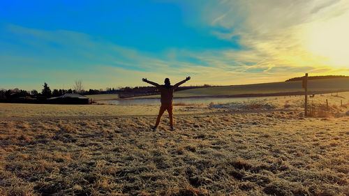 Rear view of silhouette person standing on field against sky during sunset