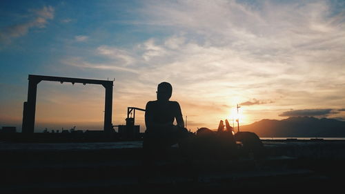 Silhouette man sitting by sea against sky during sunset