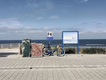 Bicycle sign on road by sea against sky
