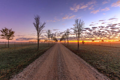 Road amidst field against sky at sunset