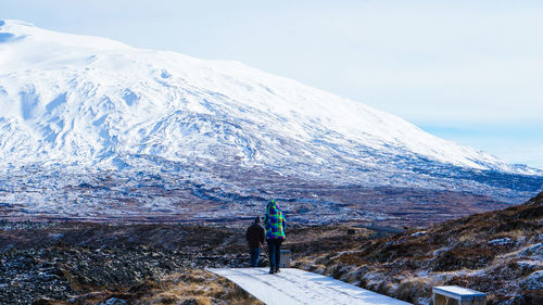 Rear view of person standing on snowcapped mountain against sky