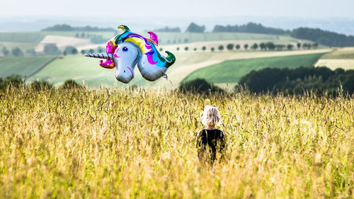 Rear view of girl holding unicorn balloon standing on field