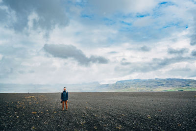 Man with camera standing on field against cloudy sky