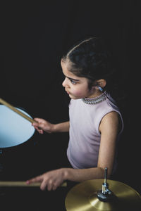 Girl playing musical instrument against black background