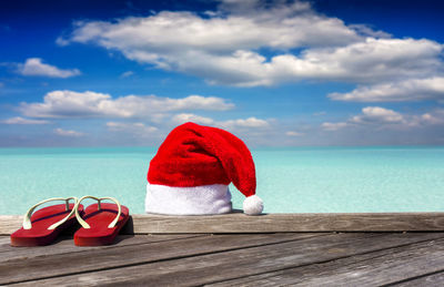 Santa hat and flip flops on jetty by sea against sky