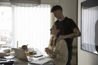 Young man massaging shoulders of girlfriend working at home