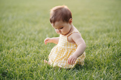 Baby girl in yellow dress sitting on grass in park outdoors. funny child toddler playing 