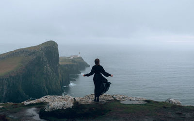 Man standing on rock by sea against sky