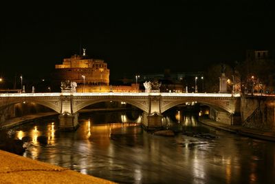 Illuminated bridge over river against building