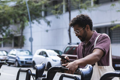 Man using smart phone while sitting on rented bicycle in city