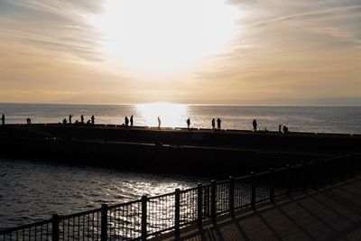 Silhouette people standing on beach against sky during sunset