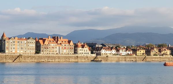 Buildings by river against sky in town