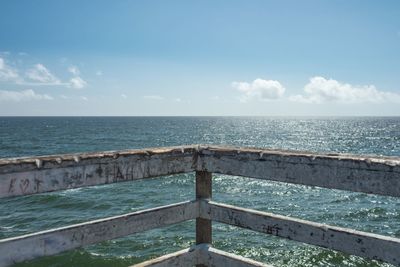 Wooden railing by sea against sky