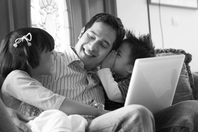 Father with children using laptop on sofa at home