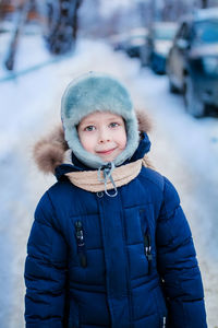 Portrait of a boy with large eyes, a warm hat and jacket, on a winter street