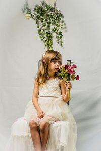 Young woman holding flower while sitting against wall