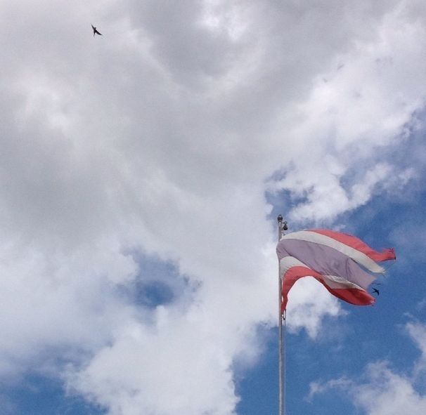 low angle view, sky, cloud - sky, flying, cloudy, cloud, flag, patriotism, identity, mid-air, national flag, wind, day, pole, red, outdoors, nature, american flag, blue, freedom