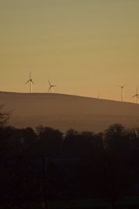 Silhouette of wind turbines against sky during sunset