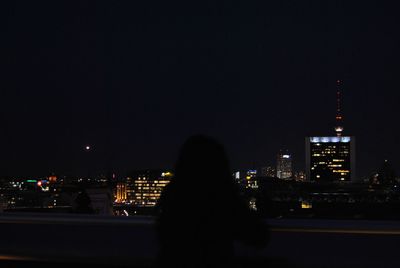 Rear view of silhouette man against illuminated cityscape at night