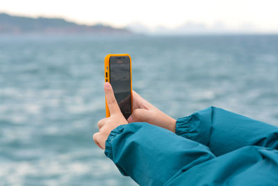 Midsection of man using mobile phone against sea