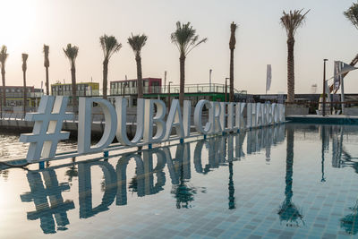 Palm trees by swimming pool in city against sky