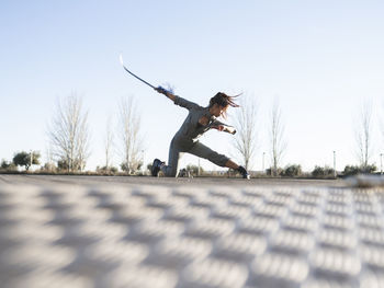 Young woman with sword practicing martial arts in park against clear sky