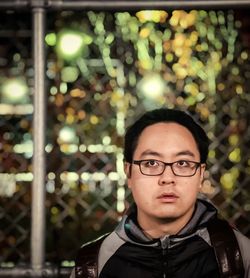 Portrait of young man wearing eyeglasses against metal fence and colorful neon lights.