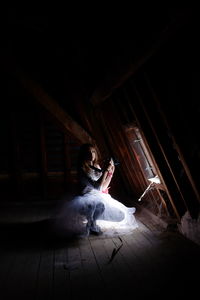 Portrait of young woman photographing while crouching by window