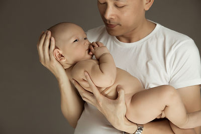 Father holding naked son against gray background