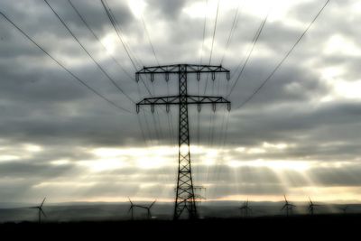 Low angle view of electricity pylon against cloudy sky