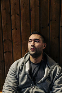 Male athlete looking away while sitting near wooden wall