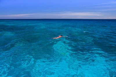 Person paragliding in sea against blue sky