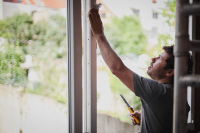 Caucasian man cleans window frames outside.